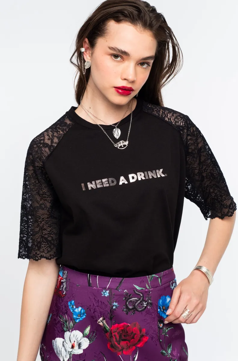 Το Icon T-Shirt συνδυάζει το διαχρονικό μαύρο βαμβακερό ύφασμα με ιδιαίτερες λεπτομέρειες από δαντέλα και ένα ξεχωριστό foil print που αναγράφει “I need a drink”.