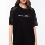 Το Icon T-Shirt συνδυάζει το διαχρονικό μαύρο βαμβακερό ύφασμα με ιδιαίτερες λεπτομέρειες από δαντέλα και ένα ξεχωριστό foil print που αναγράφει “I need a drink”.