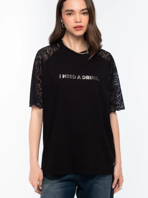 Το Icon T-Shirt συνδυάζει το διαχρονικό μαύρο βαμβακερό ύφασμα με ιδιαίτερες λεπτομέρειες από δαντέλα και ένα ξεχωριστό foil print που αναγράφει “I need a drink”.