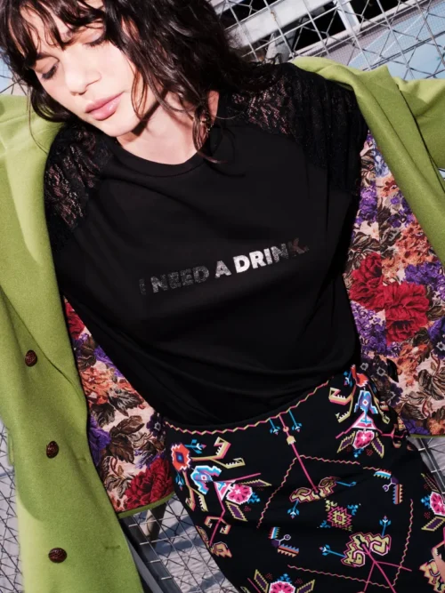 Το Icon T-Shirt συνδυάζει το διαχρονικό μαύρο βαμβακερό ύφασμα με ιδιαίτερες λεπτομέρειες από δαντέλα και ένα ξεχωριστό foil print που αναγράφει “I need a drink”.
