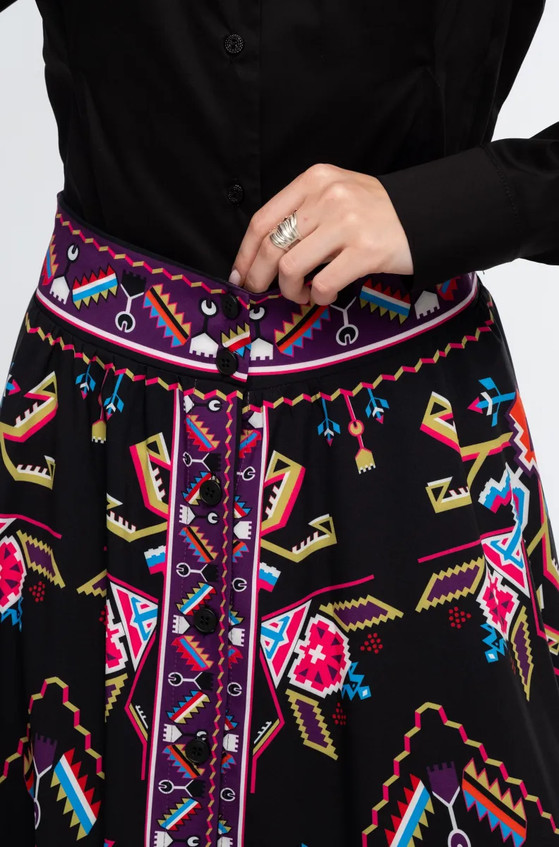Η Emblem Midi Skirt της Peace + Chaos είναι μια εντυπωσιακή midi φούστα σε A-line γραμμή, με ιδιαίτερο placement print εμπνευσμένο από ψηφιακές αναπαραστάσεις παραδοσιακών μοτίβων λαϊκής τέχνης, διακοσμητικών borders και κεντημάτων.
